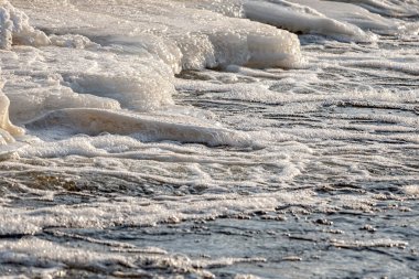 Güneş arka planda batarken dalgalar köpükle buzlu bir kıyıya vurur..