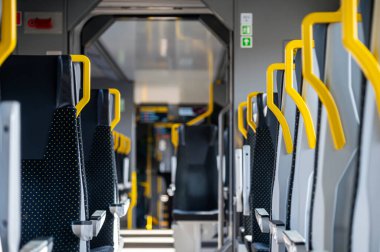 Trenin içinde boş koltuklar var. Sarı korkuluklar görülebilir..