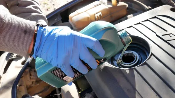 Main d'un mécanicien avec un gant bleu faisant le changement d'huile moteur Image En Vente