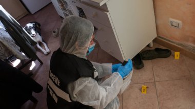 Olay yerindeki olay yeri inceleme dedektifi mavi fenerlerle inceleme yapıyor ve bir cinayetin işlendiği evin kapı kolundan alınan laboratuvara bilimsel kanıtlar götürüyor.