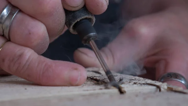 close-up of worker\'s hand with tools hacking wood with smoke that is seen from overheating of the tool