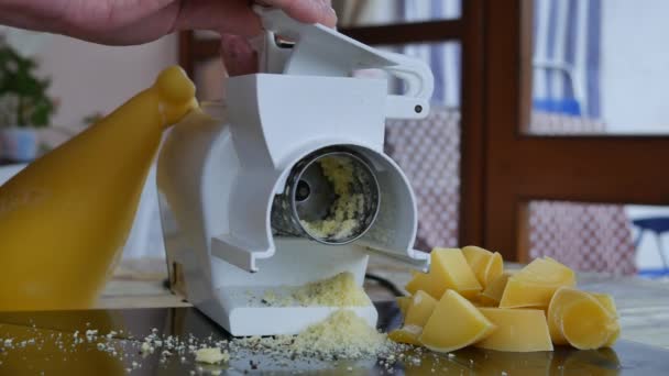 Close up de queijo parmesão ralado descendo do ralador elétrico rotativo com o fundo de uma roda de queijo apetitosa e nas laterais as peças prontas para serem raladas — Vídeo de Stock