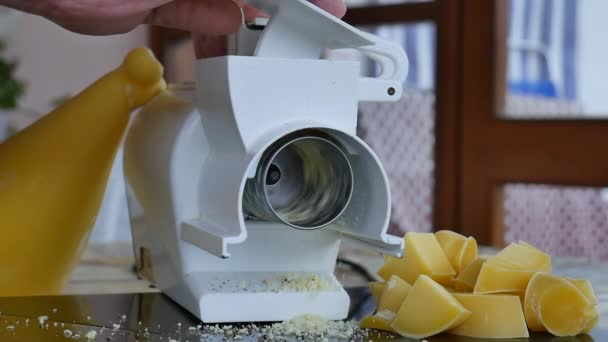 Close up de queijo parmesão ralado descendo do ralador elétrico rotativo com o fundo de uma roda de queijo apetitosa e nas laterais as peças prontas para serem raladas — Vídeo de Stock