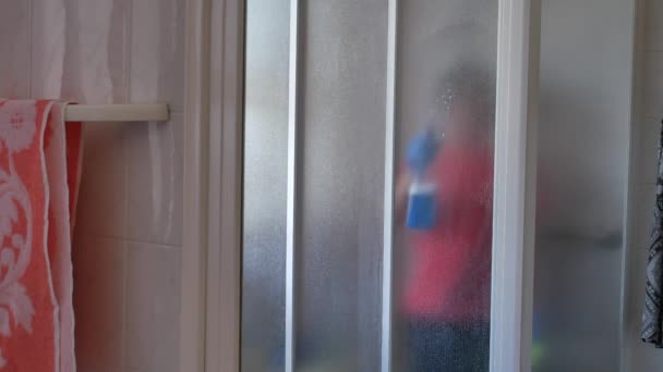 Frau desinfiziert Duschkabinenfenster mit blauem Bakterienspray gegen Viren — Stockvideo