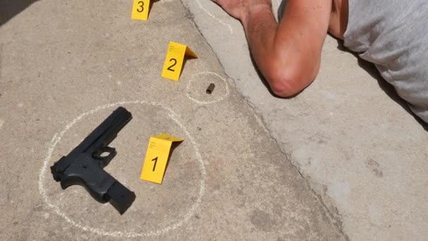Судебный инспектор собирает огнестрельные снаряды на месте преступления с мертвым мужчиной, лежащим на земле — стоковое видео