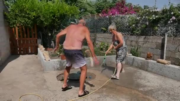 Família idosa feliz brinca com água no jardim molhando, fazendo cambalhotas e se divertindo como crianças transmitindo felicidade e alegria de viver — Vídeo de Stock