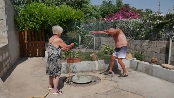 Feliz familia de ancianos juegan con agua en el jardín mojándose, haciendo volteretas y divirtiéndose como niños transmitiendo felicidad y alegría de vivir — Vídeo de stock