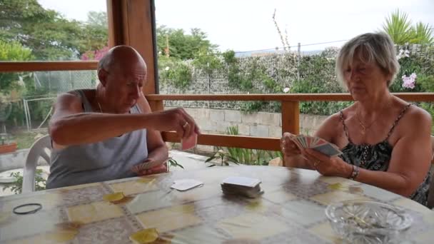 Pareja de ancianos jubilados, marido y mujer, jugar rummy en el verano, bajo un cenador en el jardín. — Vídeos de Stock