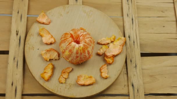 Lapso de tempo, stop motion, de uma clementina ou tangerina vista de cima com sua cor laranja intensa que é descascada, pedaço de casca um de cada vez, deixando as cunhas sozinhas. — Vídeo de Stock