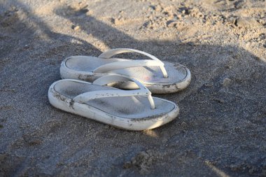 Kumlu sahil yüzeyinde dinlenen beyaz parmak arası terlikler.