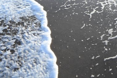 Dalgalar yavaşça kumlu sahile çarpar ve beyaz köpük oluşturur.