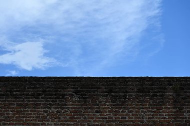 Beyaz bulutlu açık mavi gökyüzüne karşı tuğla duvar
