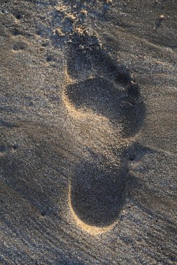 Altın saat güneş ışığında kumların üzerinde beliren ayak izleri.