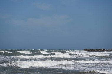 Dalgalar gökyüzünün altındaki kayalık kıyılara çarpıyor