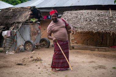 Kızıl Müslüman Takiyyah Fez Şapkalı Afrikalı yaşlı bir adam, Tanzanya 'nın Küçük Uzak Köyü' nde, Pemba Adası 'nda, Zanzibar' da çatısı Thatched olan, Yard 'da topal insanlar için sopayla poz veriyor.