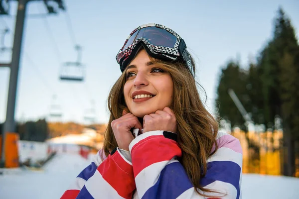 Retrato de la bella mujer caucásica feliz en traje de esquí y con máscara de snowboard en la cabeza. Retrato de mujer rubia alegre en la estación de esquí — Foto de Stock