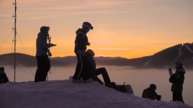 UKRAINE, BUKOVEL - Aralık 2020: Smartphone 'da Sunset Fotografları Yapan Kayakçılar Grubu kar tepenin tepesinde Ilık içecekler içiyor ve Güzel Gün Batımını izliyor