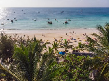 Yeşil palmiye ağaçlarının arkasındaki kumlu plajın yakınındaki bir otelde hava manzarası. Afrika, Zanzibar 'da Hint Okyanusu kıyıları