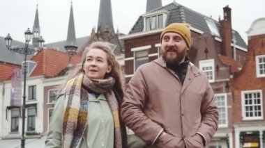 Yakışıklı çift, Hollanda 'nın Delft kentinde bahar veya sonbahar bulutlu havasında eski evlerle çevrili olarak Central Square' de yürüyor