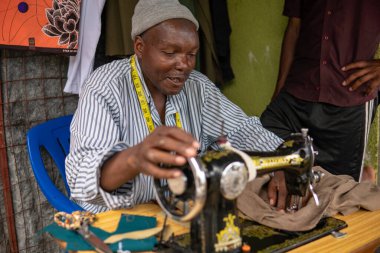 TANZANIA, MASAI VILLAGE - 2020: Arusha 'nın Maasailand ilçesindeki yerli masai köyünde dikiş makinesi ile çalışan İsviçreli Terzi Maasai' nin Kanalizasyon Portresi
