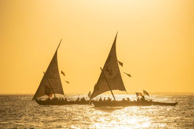 Gün batımında iki dhows mesafede. Dhow 'lar tahtadan yelkenli teknelerdir. Çoğunlukla bir yerden diğerine mal taşımak için kullanılan Hint Okyanusu' nda kullanılır.