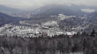 Dağlık bir köyün kışın karla kaplı tepeleri ve Çam Ormanı 'nı gösteren hava manzarası. Yaremche, Ukrayna. Karlı tepelerin ve küçük ahşap evlerin üzerinde uçuyorlar. Kırsal, köknar ağacı. Drone görünümü.