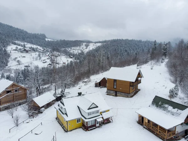 Vista aérea de un pueblo de montaña con colinas cubiertas de nieve y bosque de pinos en invierno. Yaremche, Ucrania. Volando sobre las colinas nevadas y pequeñas casas de madera. Campiña, abeto. Vista del dron — Foto de Stock