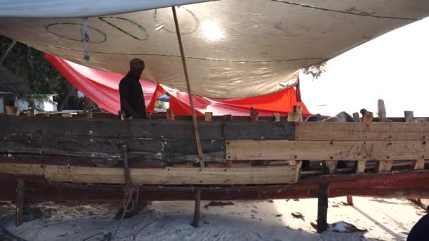 Ciudad de piedra, Zanzíbar, Tanzania - Enero 2020: Hombres africanos arreglan el barco pesquero de madera Dhow en la costa — Vídeo de stock