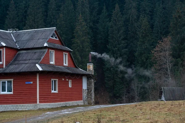 Humo blanco de las chimeneas de casas de madera precisas en un pueblo de montaña en otoño sobre un fondo de bosque y montañas — Foto de Stock