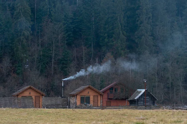 Humo blanco de las chimeneas de casas de madera precisas en un pueblo de montaña en otoño sobre un fondo de bosque y montañas — Foto de Stock