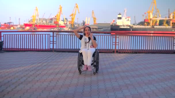 Fröhlich Nettes Mädchen im Rollstuhl in lässigem Outfit sitzt auf dem Broadway im Seehafen in Odessa — Stockvideo
