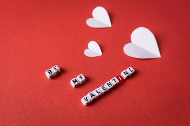 Kırmızı zemin üzerinde beyaz kağıt kalpler olan kare boncuk harflerle yazılmış sevgililer günü mesajım ol.