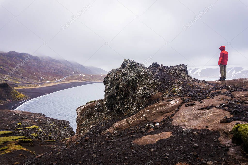 Tourist standing on a rock and looking at black beach of Lake Kleifarvatn near Krysuvik in Iceland