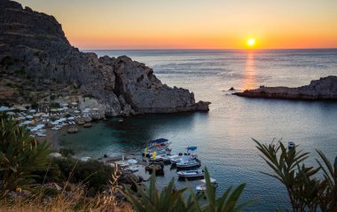Lindos, Rodos, Yunanistan 'da tekneleri olan Saint Paul Körfezi plajı, yükselen güneşli güzel deniz manzarası