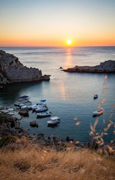 Saint Paul\'s Bay beach with boats in Lindos, Rhodes, Greece at sunrise. Rising sun between two cliffs