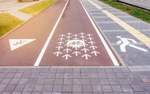 Cycle lane, running track and a pavement. Cycle path marked with signs and arrows painted on red asphalt