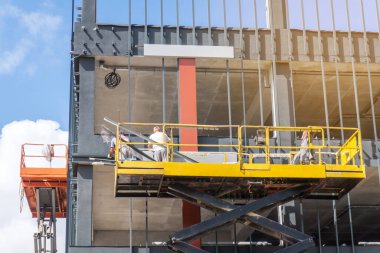 Bir inşaat sahasında makas kaldırma platformundaki inşaatçılar, yeni bir ticari binanın ön cephesi üzerinde çalışıyorlar.