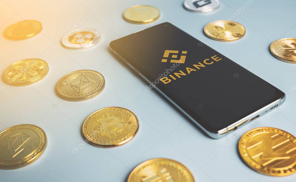 Binance app logo on a smartphone among crypto coins on blue background. Popular cryptocurrency exchange. Swansea, UK - August 29, 2021.
