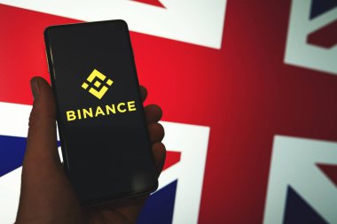 Birleşik Krallık bayrak arkaplanlı Binance simgesi telefonda