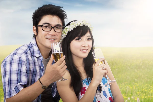 Asiatiska par njuta av champagne på fältet — Stockfoto