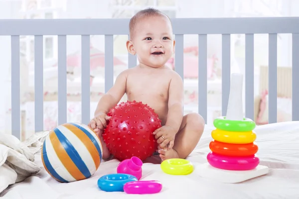 Cheerful baby playing with toys in baby crib — Stock Photo, Image