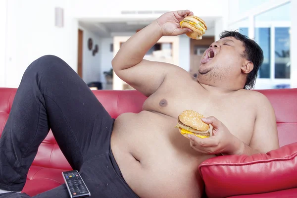 Hungry overweight person eats burger at home — Stock Photo, Image