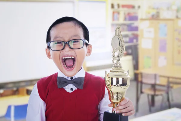 Estudante animado menino segurando troféu na biblioteca — Fotografia de Stock