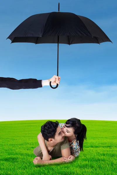 Happy couple lying on grass under umbrella — Stock Photo, Image