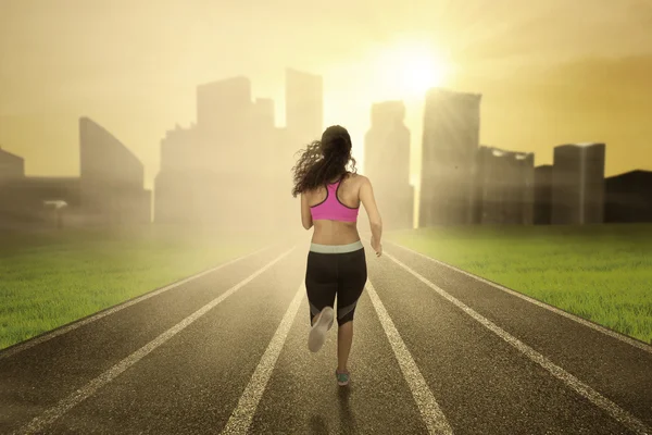 Fitnessfrau rennt auf Feld in Richtung Stadt — Stockfoto
