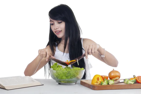 Mulher faz salada enquanto lê livro — Fotografia de Stock