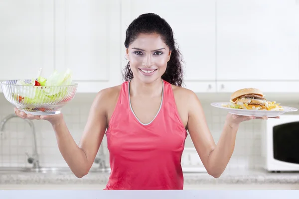 Mulher segura salada e hambúrguer na cozinha — Fotografia de Stock