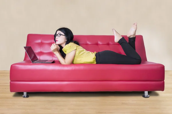 Chica soñando despierto en el sofá con el ordenador portátil —  Fotos de Stock