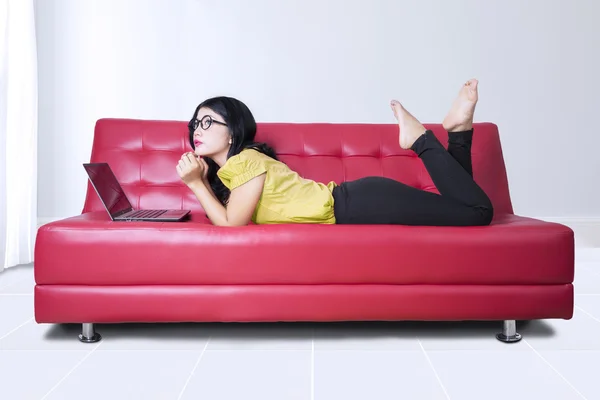 Frau mit Laptop auf rotem Sofa zu Hause — Stockfoto