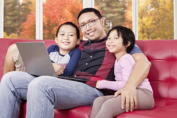 Hombre joven sentado en el sofá con sus hijos y portátil — Foto de Stock